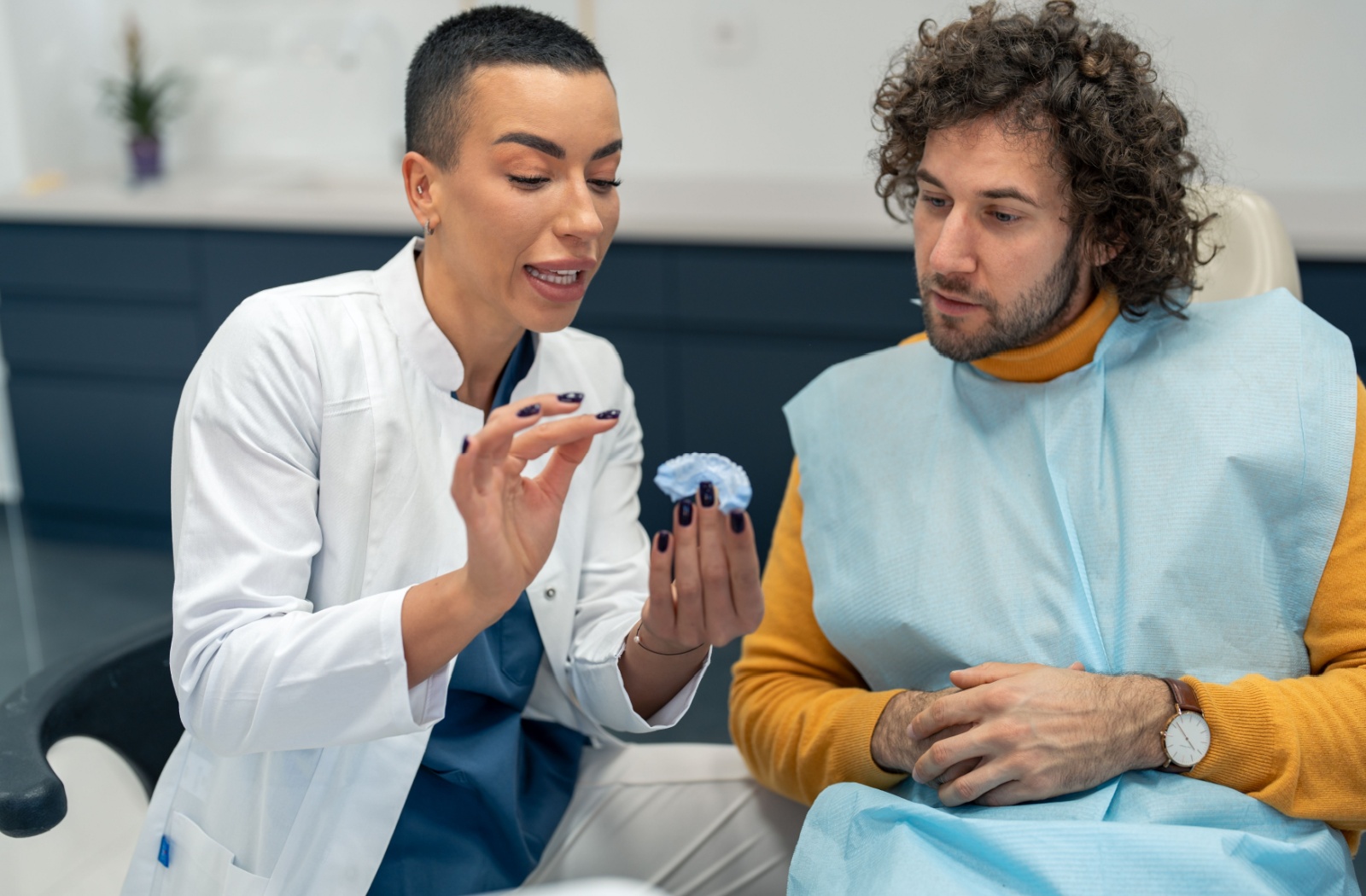 A dentist uses molds to explain how take-home dental strips target discolouration during their patients' teeth whitening consultation.