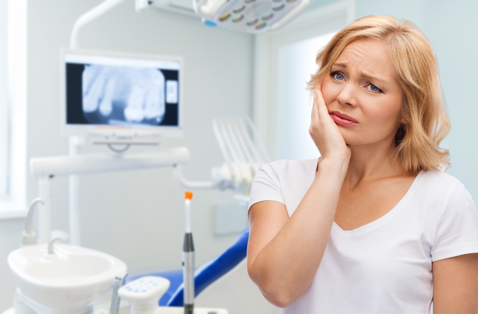 Person at dental office holding cheek experiencing unexplained jaw or tooth pain with X-ray monitor in background
