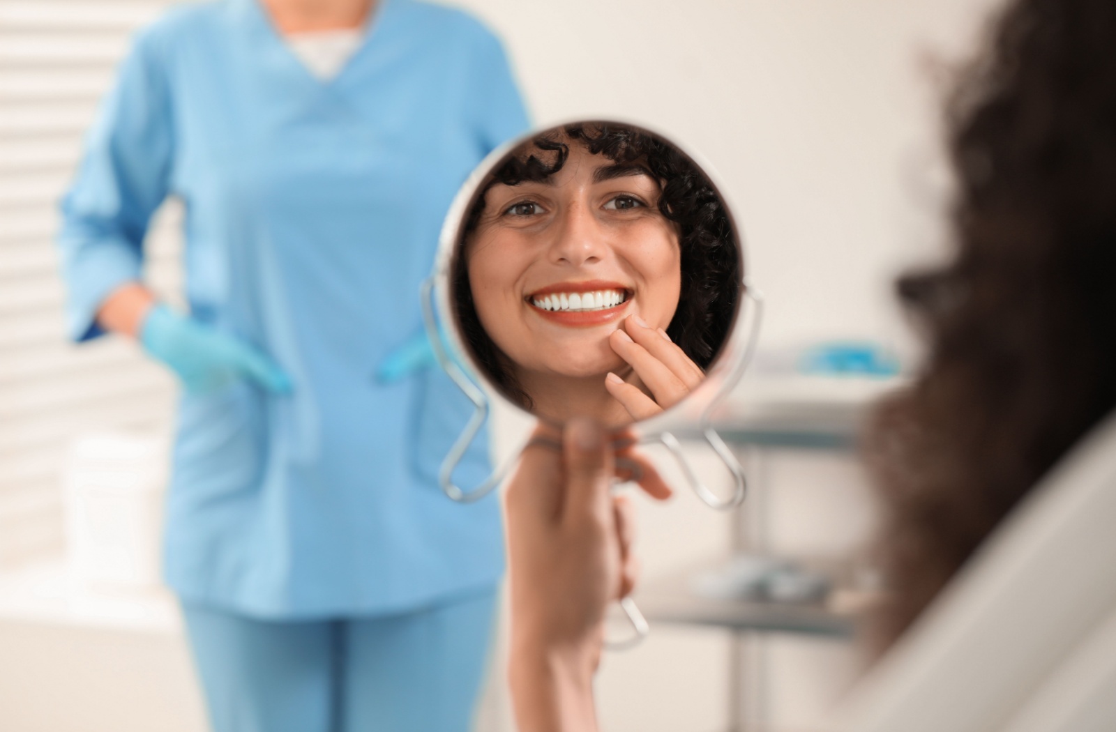 Patient smiling while looking at their teeth in a mirror after receiving a dental crown.